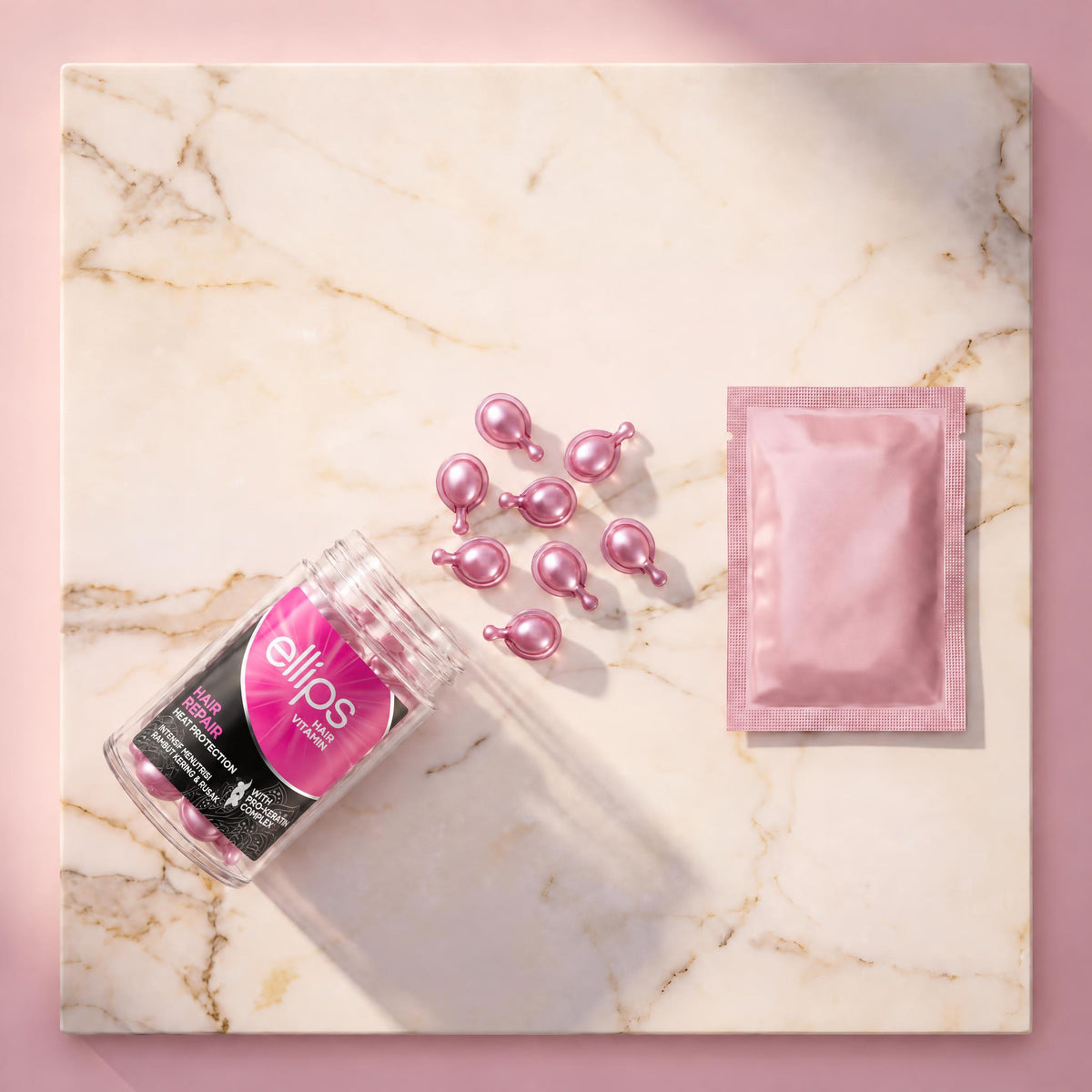 Top view of an open Ellips Hair Repair jar with pearly pink capsules and a pink sachet on marble