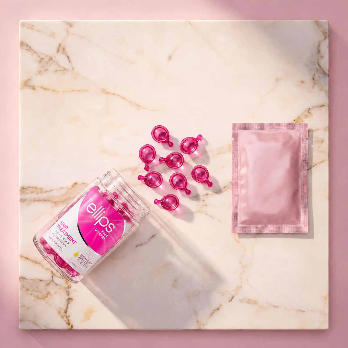Top view of an open Ellips Hair Treatment jar with magenta-pink capsules and a pink sachet on marble