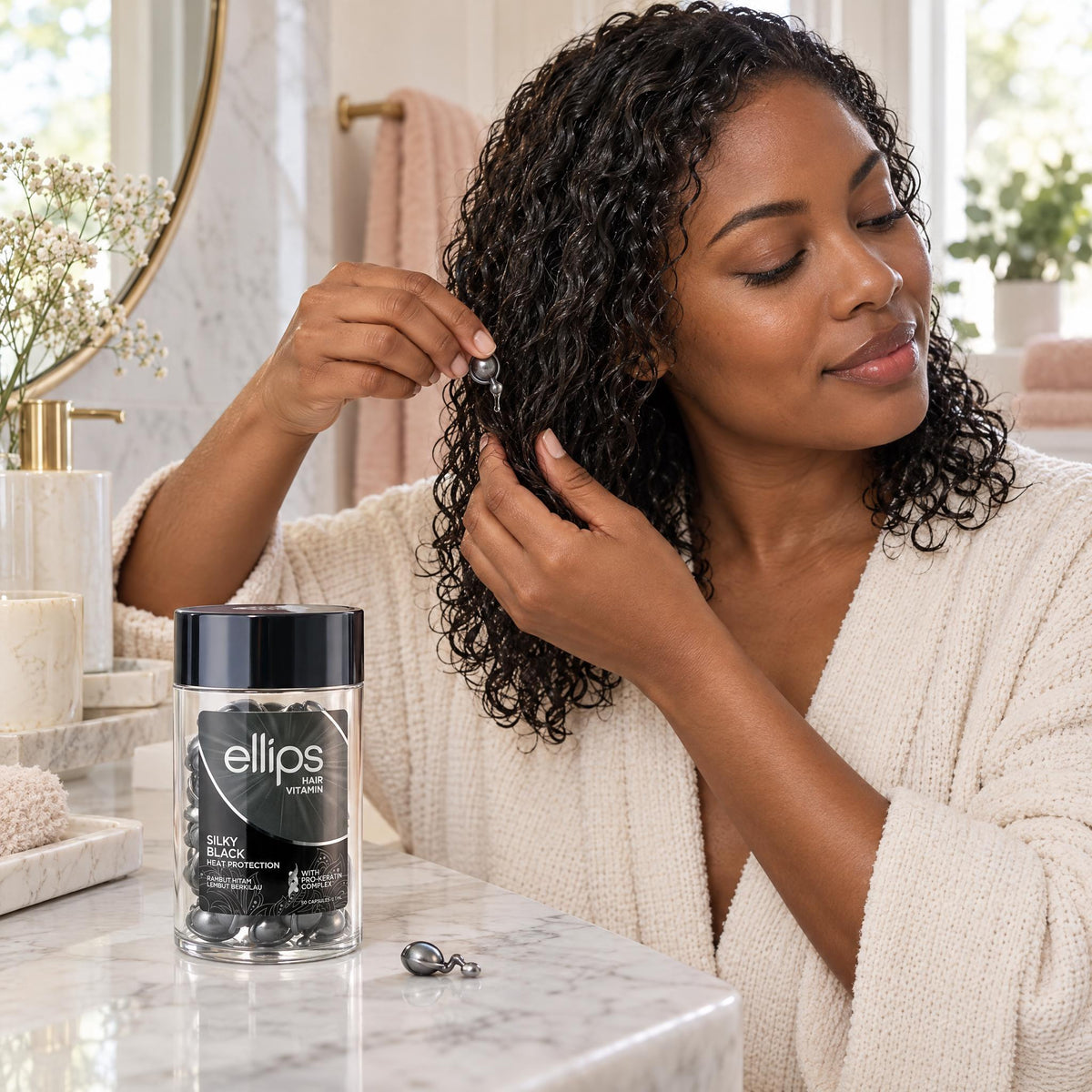 Woman working Ellips Silky Black oil through damp lengths, jar on the bathroom counter