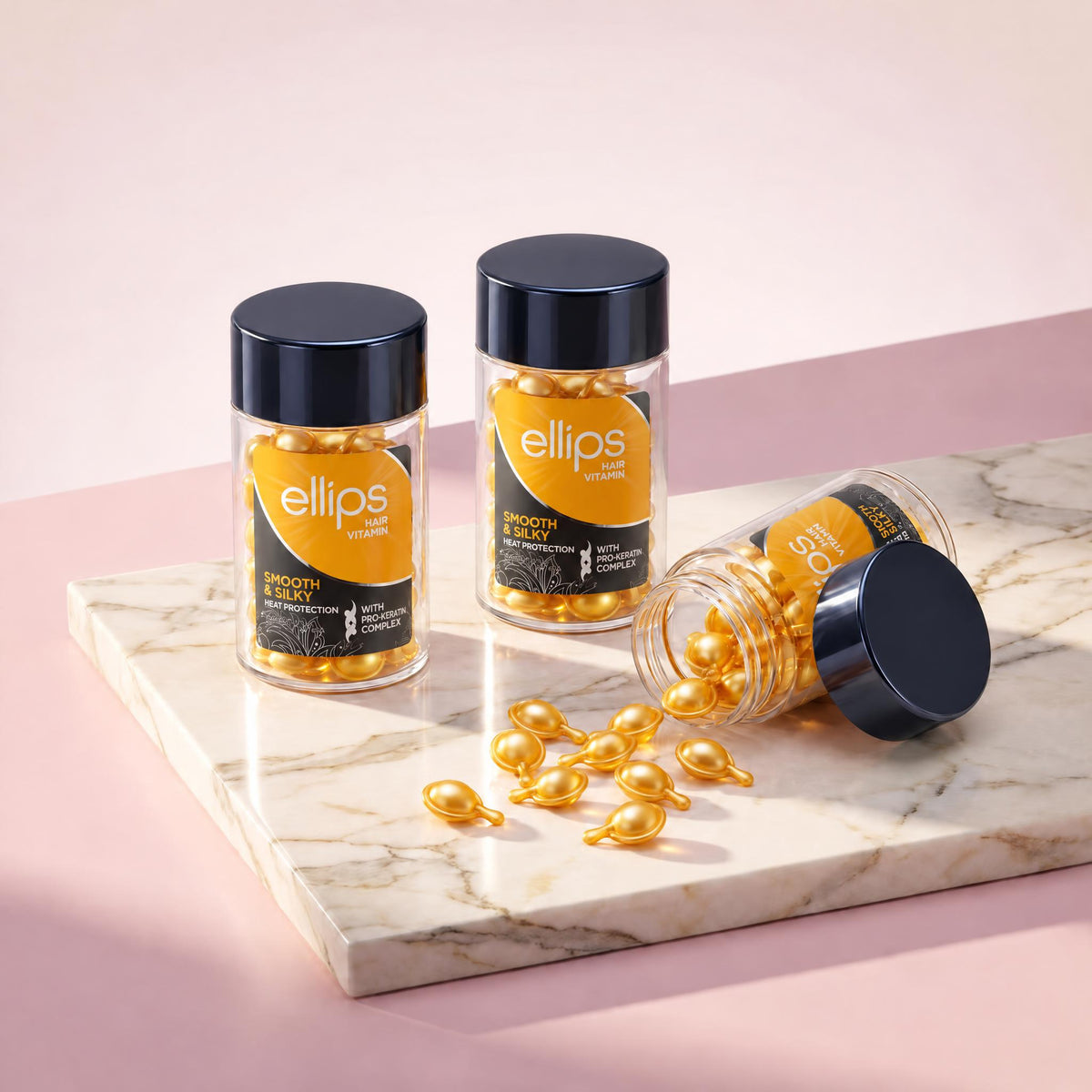 Ellips Smooth & Silky jars on marble, pearly golden capsules spilling from an open jar