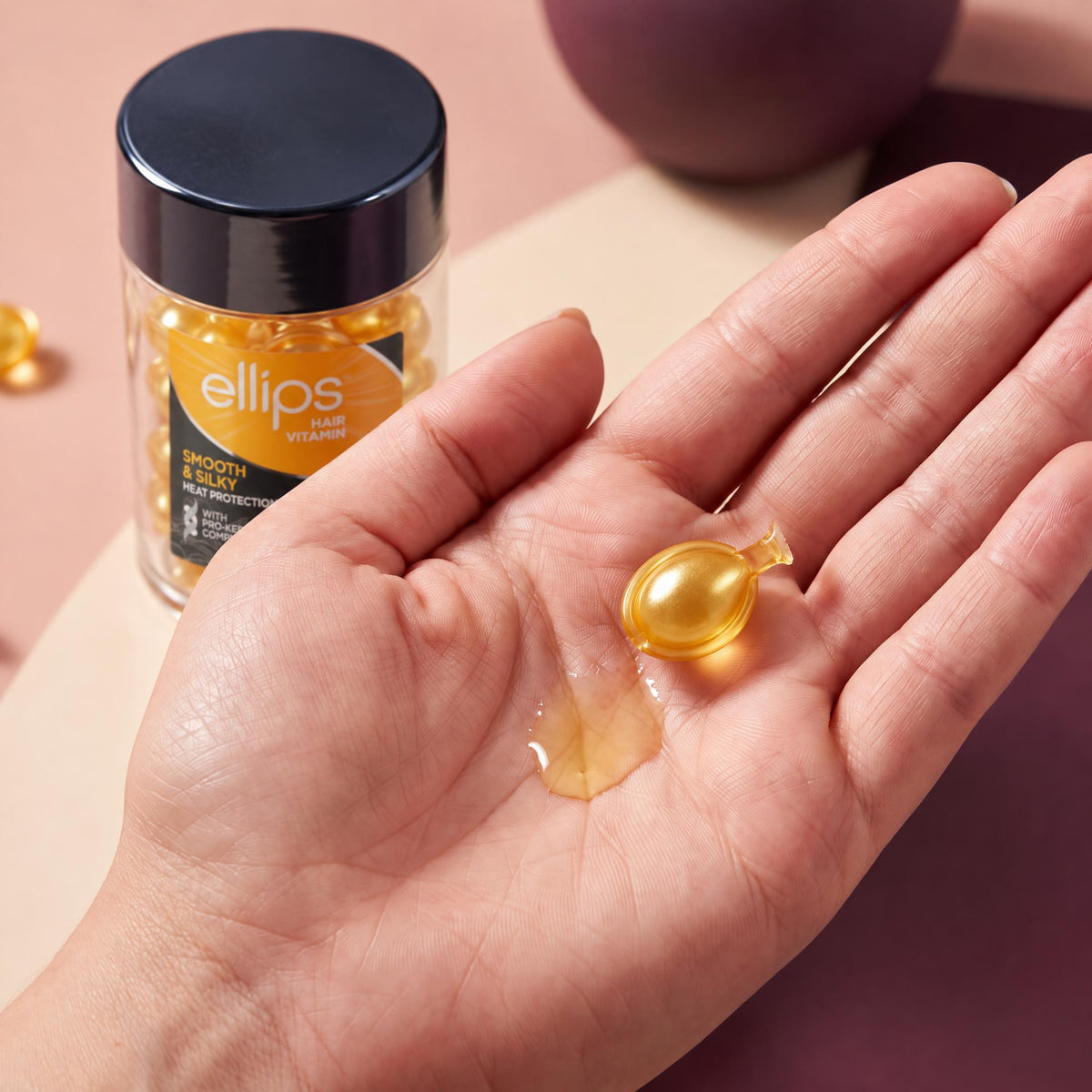 An Ellips Smooth & Silky capsule twisted open in the palm next to its oil