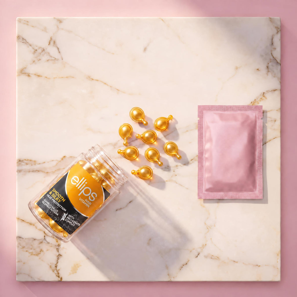 Top view of an open Ellips Smooth & Silky jar with pearly golden capsules and a pink sachet on marble